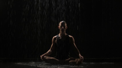 footage of man doing yoga on black backgound at night at the rain. Handsome muscular guy in shorts and t-shirt raises his arms up. Businessman on vacation.