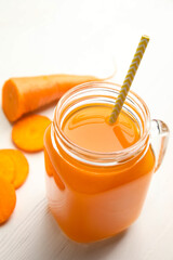 Freshly made carrot  juice in mason jar on white wooden table, closeup