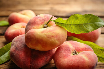 Fresh ripe donut peaches with leaves on wooden table, closeup