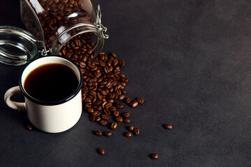 Black delicious coffee in an iron mug, jar and scattered grains on a stone table. Authentic drink, copy space.