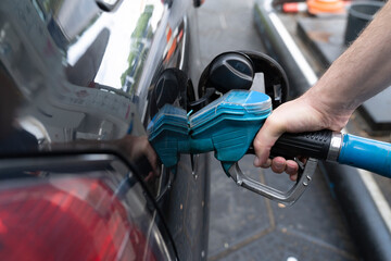 Male hand fills car with gasoline at the gas station holding a gaspump nozzle