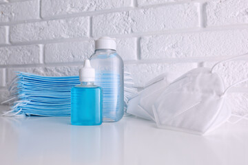 Hand sanitizers and respiratory masks on table near white brick wall. Protective essentials during COVID-19 pandemic