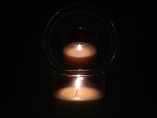 Burning white candle reflected in the mirror in the dark