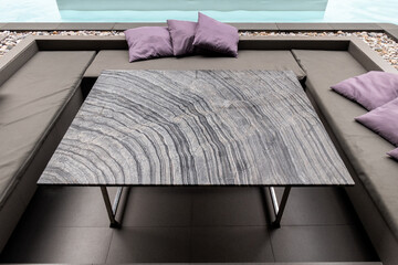 Striped granite dining table with pillow on sofa at side swimming pool
