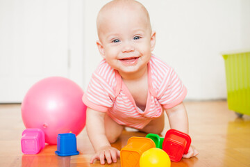 Little baby girl sitting on the floor, crawling and playing with brightly colored educational toys