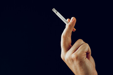 Male hand with a burning cigarette against black background