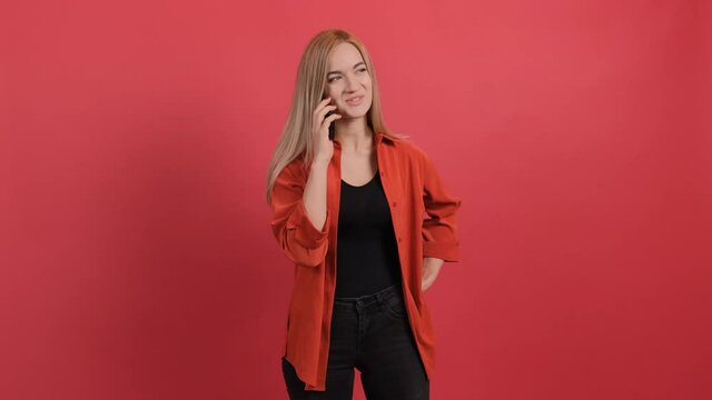 Portrait of happy young woman having a pleasant mobile conversation, isolated on red background