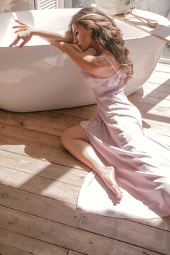 young glamour girl is laying near white bath near window in the boho style bathroom background in sun lights, morning lifestyle concept, free space