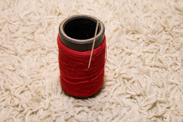 A spool of red thread with a needle lies on a white background