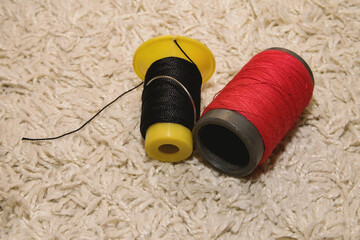 Two spools of red and black thread with a needle lies on a white background