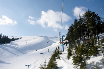Fototapeta na wymiar Ski piste and chair lift with snow covered trees on sunny day. Combloux ski area, French alps