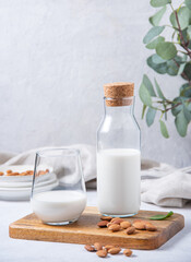 a glass and bottle of fresh vegan almond milk and a few scattered nuts on a white wooden background