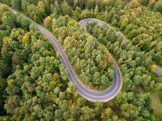 Winding road through the forest, from high mountain pass, in autumn season. Aerial view by drone. Romania