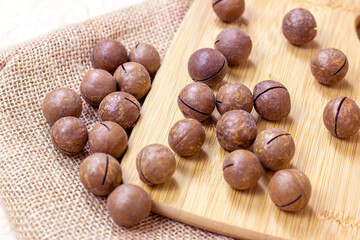 Brown macadamia nuts with wooden cutting board on light textile background.