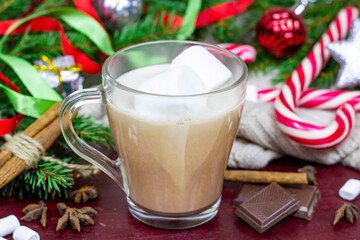 Hot chocolate Christmas and New Year celebration cocoa drink in a glass cup with fir tree branches, holiday decorations and sweet red striped lollipops on wooden background.