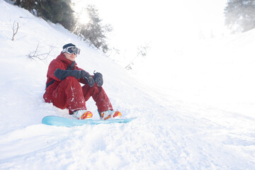 Fototapeta na wymiar winter, leisure, sport and people concept - snowboarder sits high in the mountains on the edge of the slope and looks into the distance.