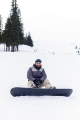 winter, leisure, sport and people concept - Snowboarder sitting at the top of a mountain and enjoying scenery