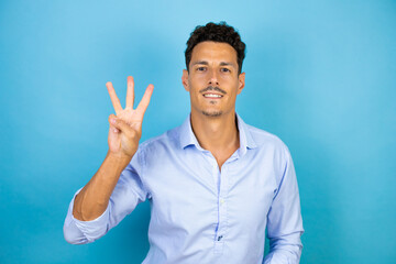 Naklejka premium Young handsome man wearing blue shirt over isolated blue background showing and pointing up with fingers number three while smiling confident and happy