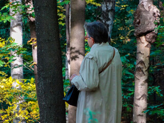 An elderly woman of 70 years touches the bark of trees in the autumn city Park, illuminated by the sun.