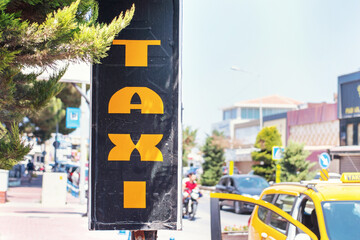 taxi vertical inscription on black sign board at city street in summer day