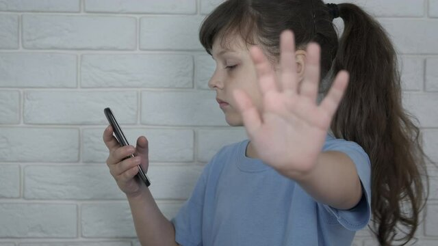Child stop chatting. Little girl with smartphone shows no gesture. Childhood smartphone addiction.