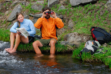 Hikers with feet in a stream checking directions with map and binoculars