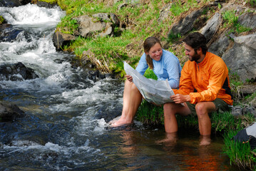 Laughing hikers check a map while soaking feet in stream