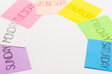 Sheets of paper of different colors are arranged in an arc. Each piece of paper has the name of one day of the week written on it.