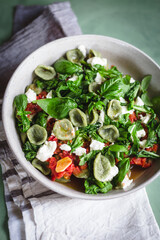 Green orecchiette with arugula tomato sauce and goat cheese on a green surface