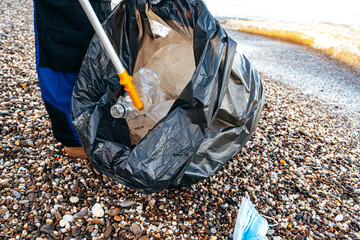 Close up photo of a man collecting garbage with a grabbing tool on the beach