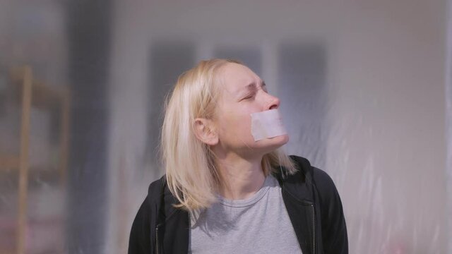 Female hostage sitting on a chair in a room with her mouth taped shut