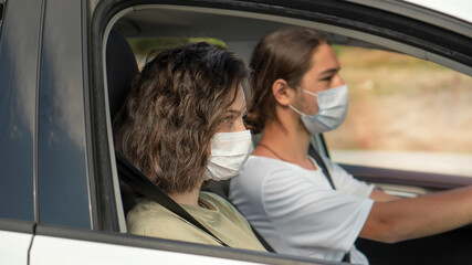Young couple wearing protective face mask are sitting in the car. Corona virus pandemic concept.Road trip in new normality.