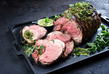 Traditional English barbecue lamb roast sliced with mint leaf and sauce offered as close-up in a...