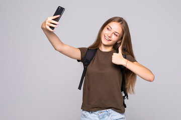 Naklejka premium Happy cheerful young woman showing thumb up and making selfie on smartphone isolated on white background