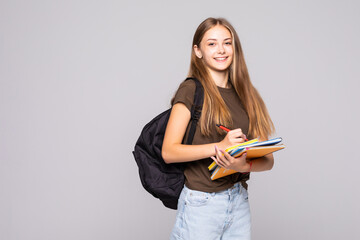 Portrait of a happy woman student with backpack writing in a notepad while standing with books...