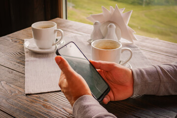 Mens hands hold a smartphone. Reads the news, dials a message at a table in the cafe with a cup of coffee or tea.
