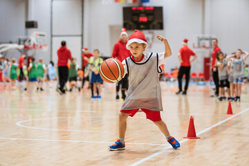 Young boy with Santa Clause hat exercises with a basketball ball in a sports hall