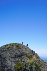 People at the top of a rocky mountain on a sunny day with a cloudless sky