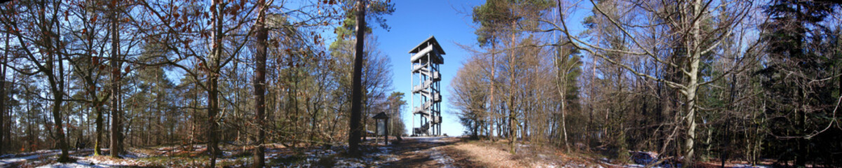 Panoramic view of a wooden lookout tower in a winter forest with snow covered trees in the Eifel...