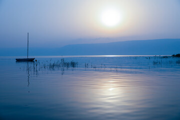 Sunrise over the lake. Boat floating on the calm water under amazing sunset.