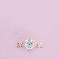 White alarm clock and numbers 2021 are decorated with golden star confetti on pastel background. Minimal concept of celebrating Christmas and New Year. Square orientation