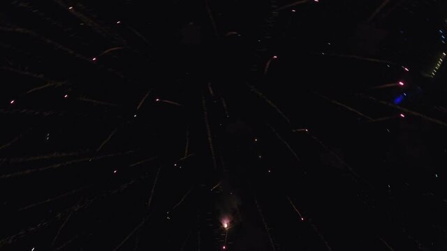 Multicolored fireworks explode in night sky, wide aerial