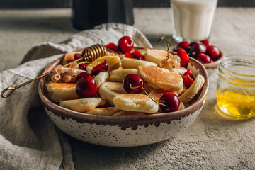 Trendy home breakfast with tiny pancakes, honey and cherries on a concrete table.
