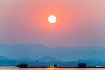 Beautiful nature landscape orange sun in the red sky sunlight over water lake blue mountain background at sunset, silhouette fish farm cages rural lifestyle at Krasiao Dam, Suphan Buri, Thailand