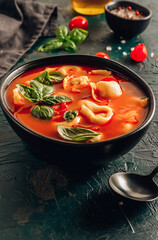 Tomato soup with tortellini in black bowl on dark background.