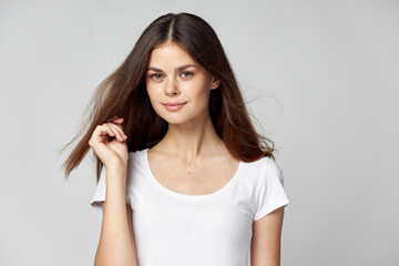 A pretty brunette in a white T-shirt holds her hand near her face and smiles 