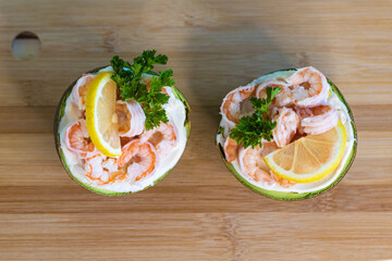 Avocado halves with shrimps and parsley on a wooden surface, top view.