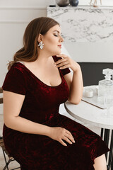 Young fat woman with bright makeup and trendy earrings in a velvet dress in the living room....