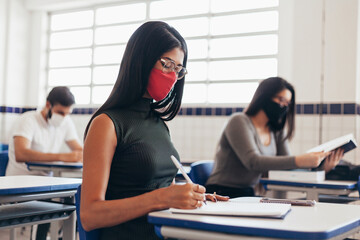 Brazilian college students wearing face masks sitting at the desk in the classroom. Concept of...