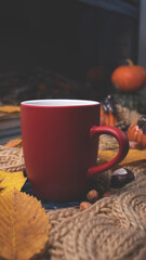 Red mug with tea on the background of a soft, knitted scarf, autumn leaves, pumpkin. Autumn background, cozy evening, fireplace.
